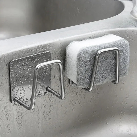 Stainless steel kitchen sink sponge holder mounted on a wet sink wall, holding a scrub sponge. Rust-resistant and durable for efficient organization.